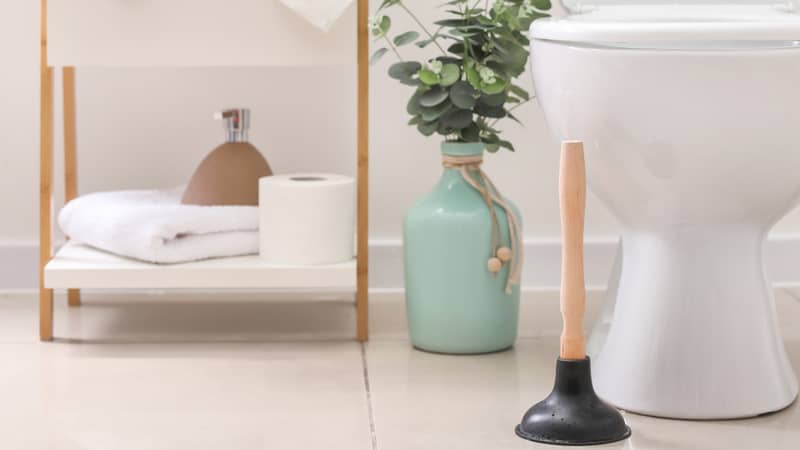 Plunger near toilet bowl in bathroom