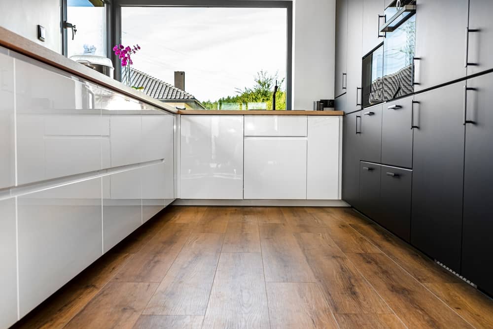 A modern kitchen with white and black fronts and a large corner window, with hybrid floors.