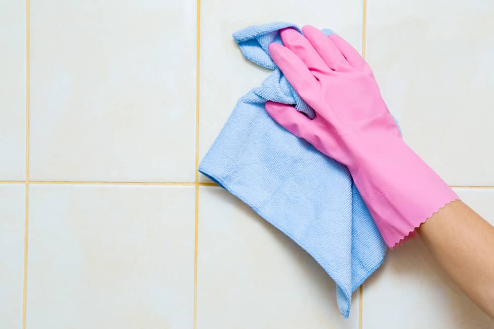 Hand in pink protective glove cleaning tiles with rag.