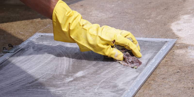 woman's hands with gloves scrubbing a removable fly screen outside