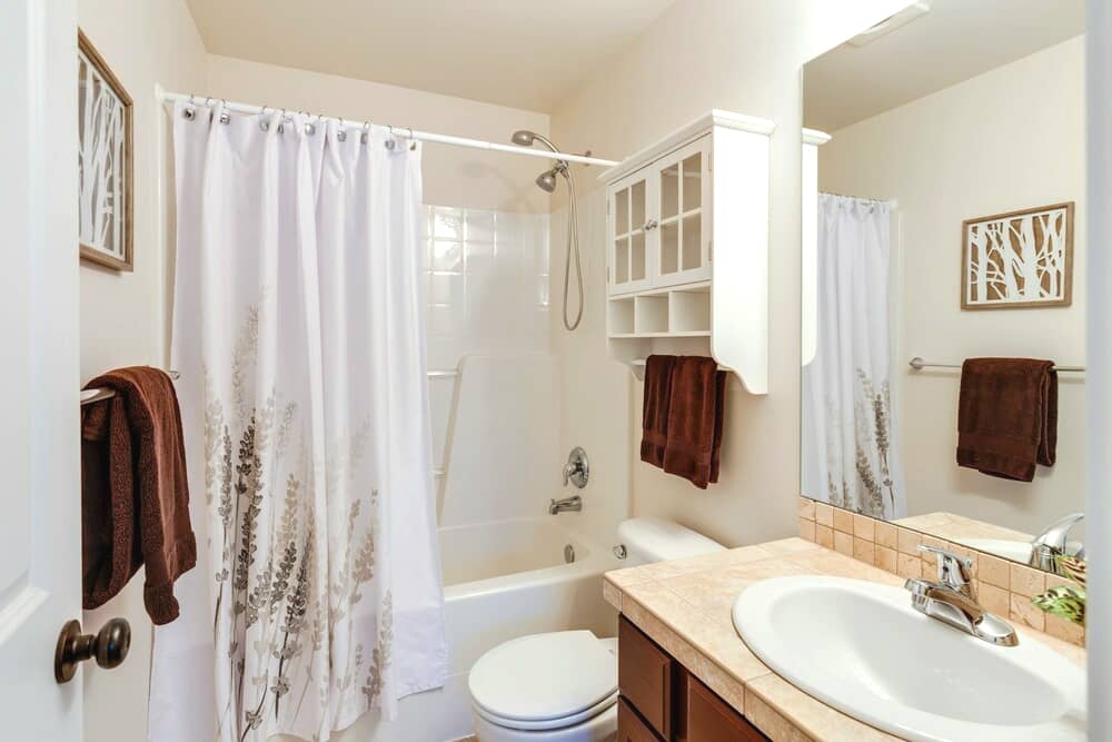 Clean bathroom with white shower curtain, brown towels, and a vanity area