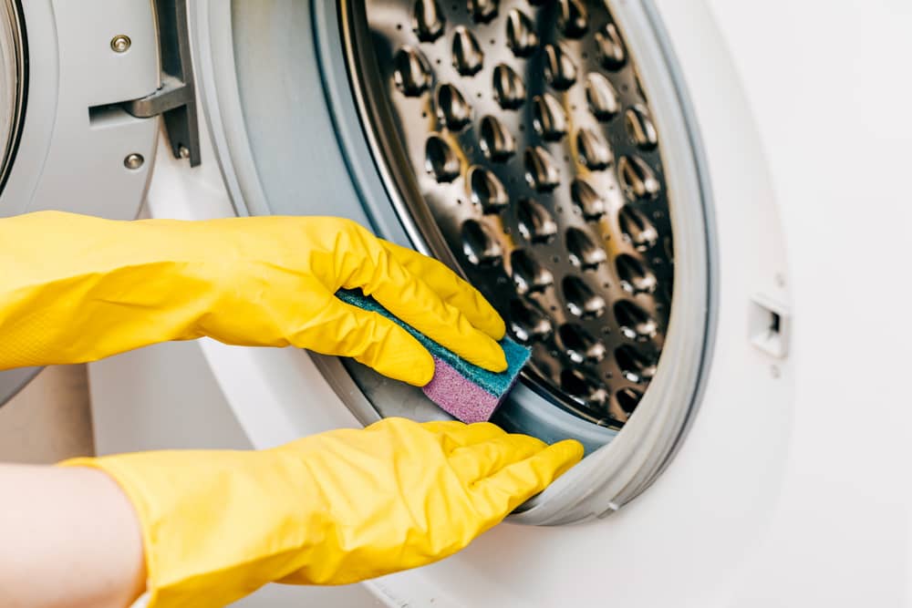 A man in yellow gloves cleans a dirty, moldy rubber seal on a washing machine. Mold, dirt, limescale in the washing machine. Periodic maintenance of household appliances.