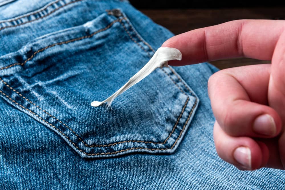 Woman hand pulling gum on jean fabric.