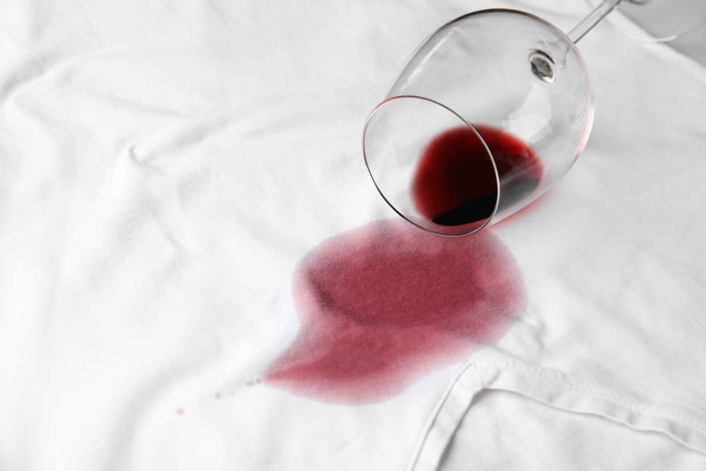 Overturned glass and spilled exquisite red wine on white t-shirt