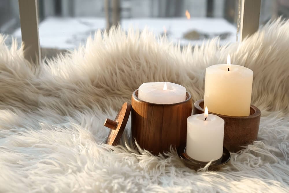 White candles in wooden holders placed on a fluffy rug by a window