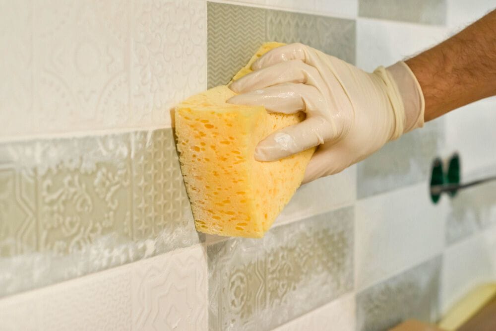 hand with gloves holding a sponge for cleaning grout haze from tiles