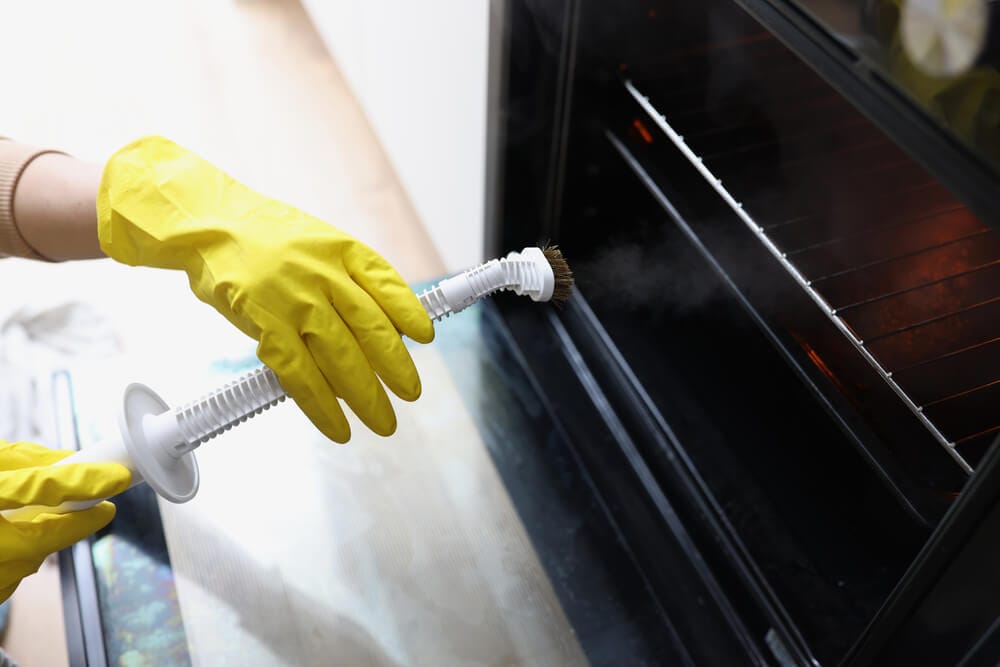 Hand wearing yellow gloves steam cleaning an oven