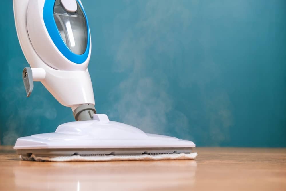 Close up of a white steam mop head emitting steam against a wooden floor