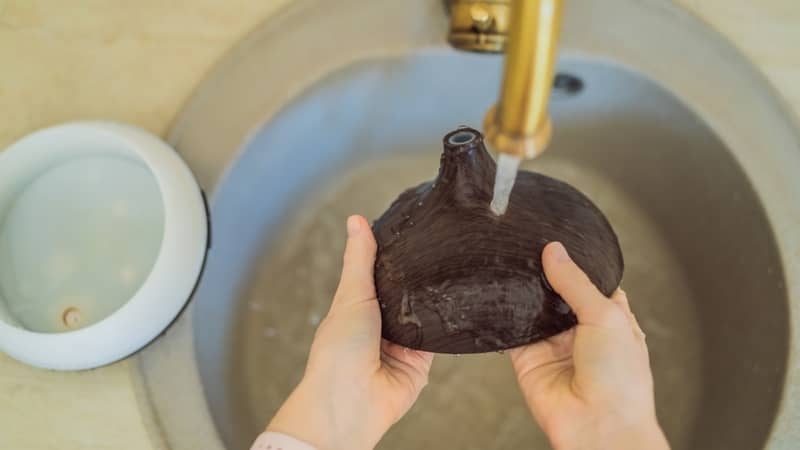 Woman washing aroma diffuser in faucet.