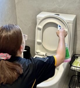 Maid2Match professional cleaner spraying a toilet cleaner on the toilet seat to clean it