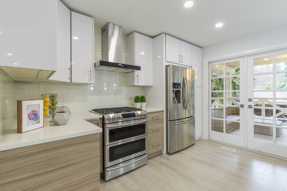 Modern kitchen interior with gas range, stainless steel fridge, white marble countertop.