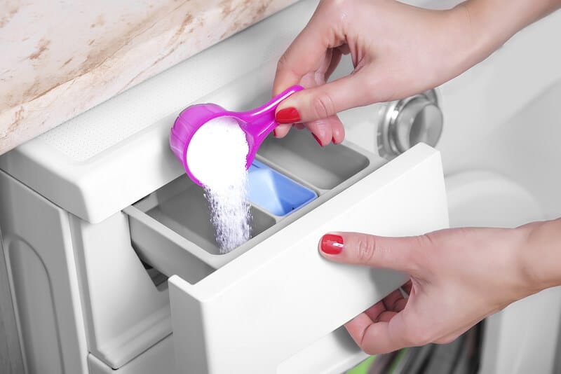 woman's hands pouring laundry detergent powder into a front load washing machine