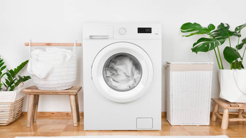 Modern washing machine, laundry in baskets and domestic room interior