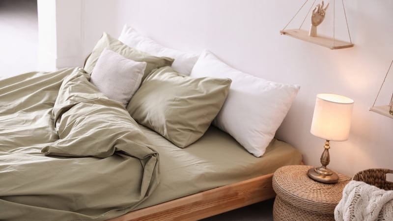 Comfortable bed with olive green linen in modern room interior