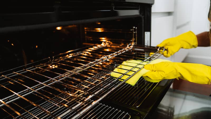 female hands with yellow gloves cleaning the oven