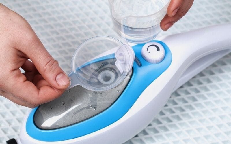 person pouring water into a container of a steam mop