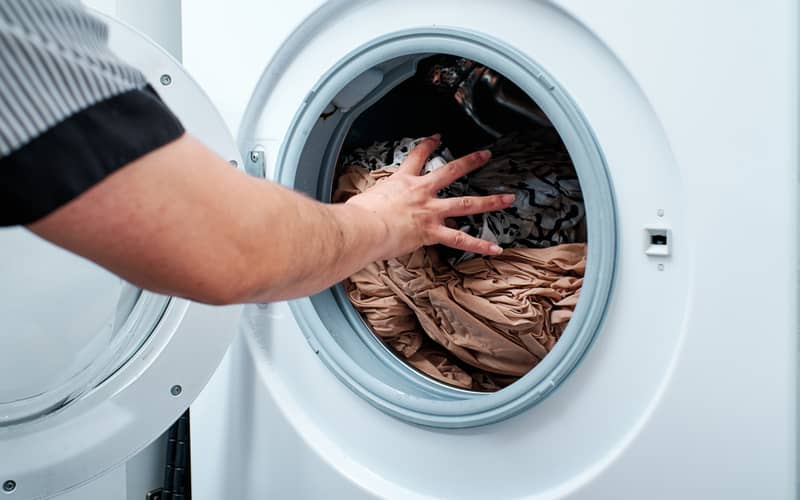 Person's hand inside the dryer with wet clohes