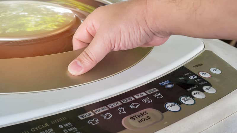 man's hand on a top loading washing machine