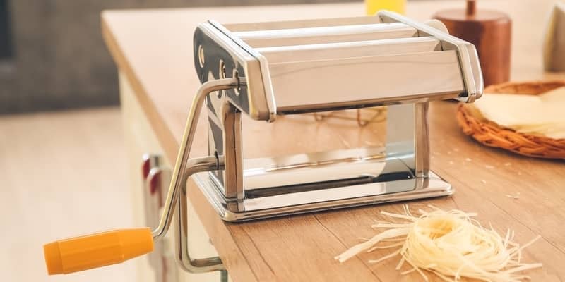 Pasta maker with dough on table in kitchen