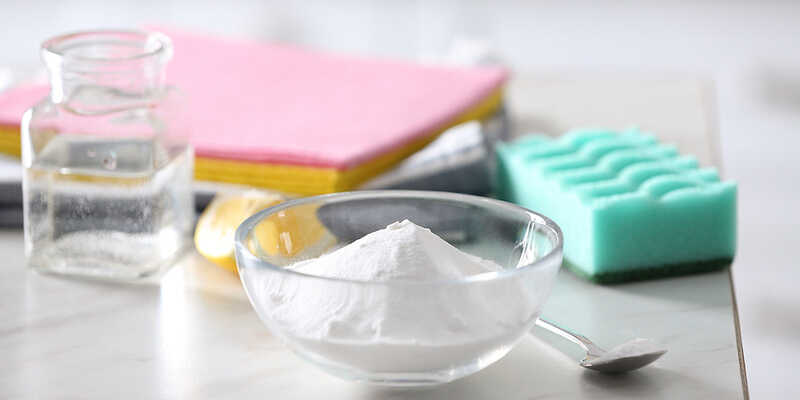 baking soda, vinegar, lemon, sponge and cloths on a white table