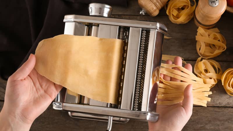 Woman making noodles with pasta machine at table, top view