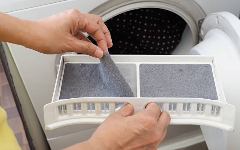 Person’s hand removing lint from filter of a tumble dryer