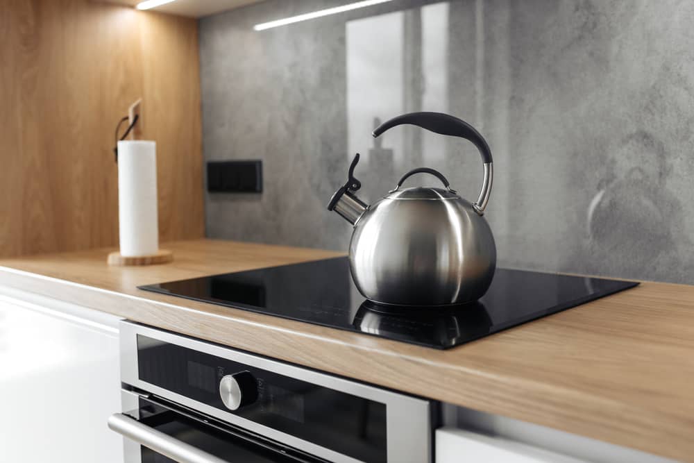 Photo of gray stainless steel kettle on the induction cooktop in the kitchen.