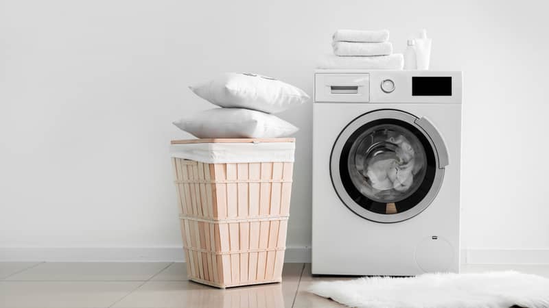 Modern washing machine with laundry near light wall