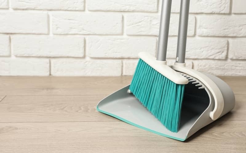 plastic broom with dustpan near white brick wall indoors