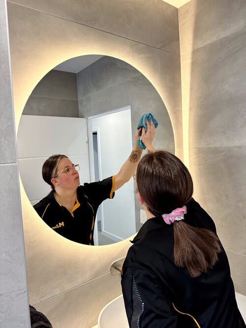 professional cleaner cleaning a circular mirror in the bathroom