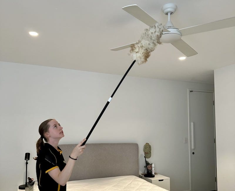 professional cleaner using a duster with extendable wand to clean a fan