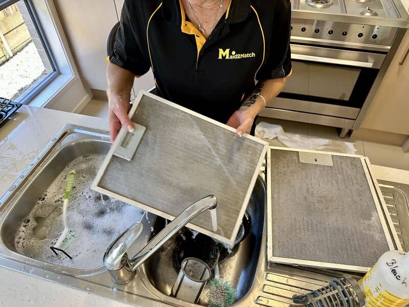 professional cleaner washing range hood filters in the sink