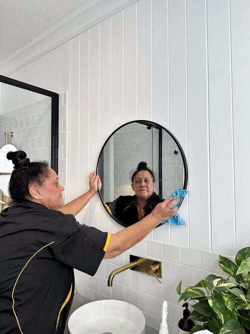 Experienced cleaner wiping around the edge of a mirror