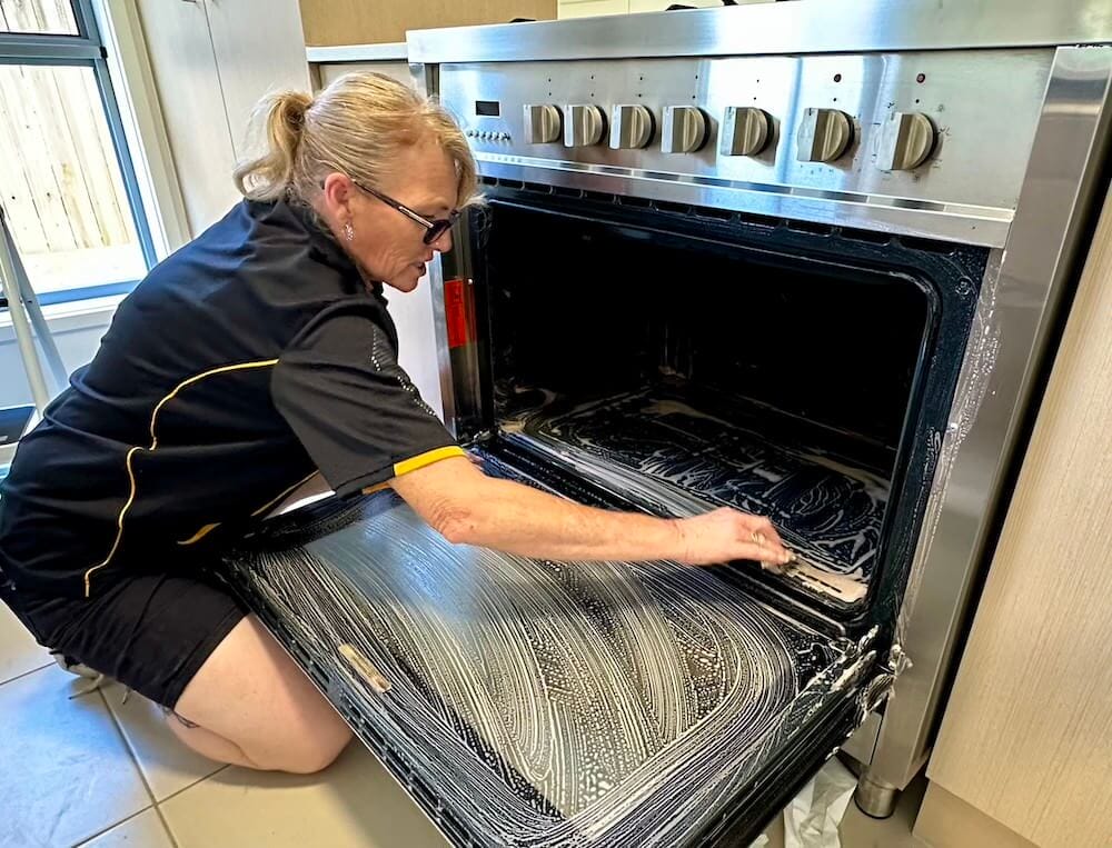 professional house cleaner using oven cleaners to clean the oven at a customer's house