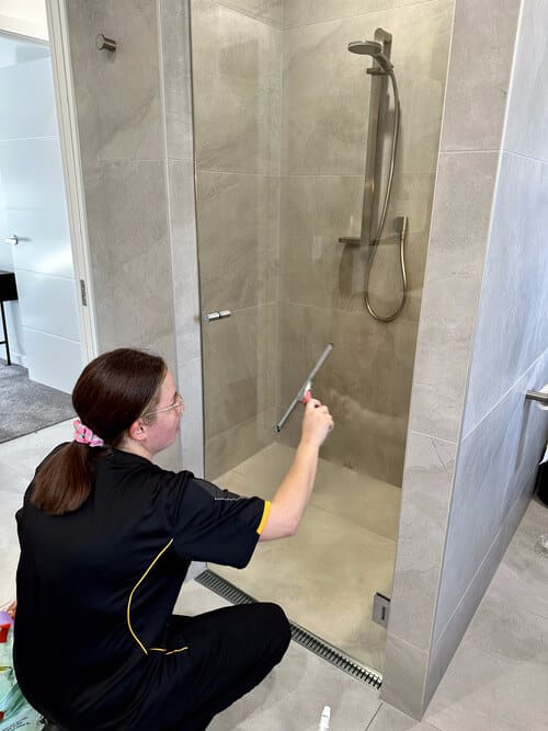 professional using squeegee to remove water droplets on shower glass