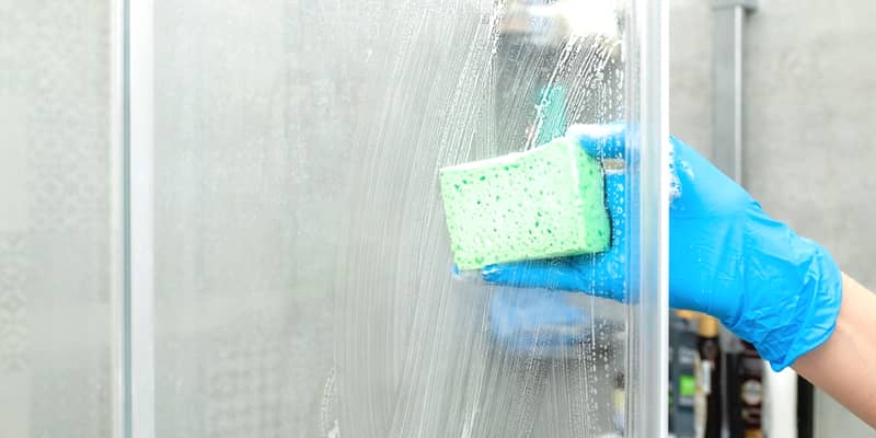 Woman in a blue glove cleans a shower screen from limestone