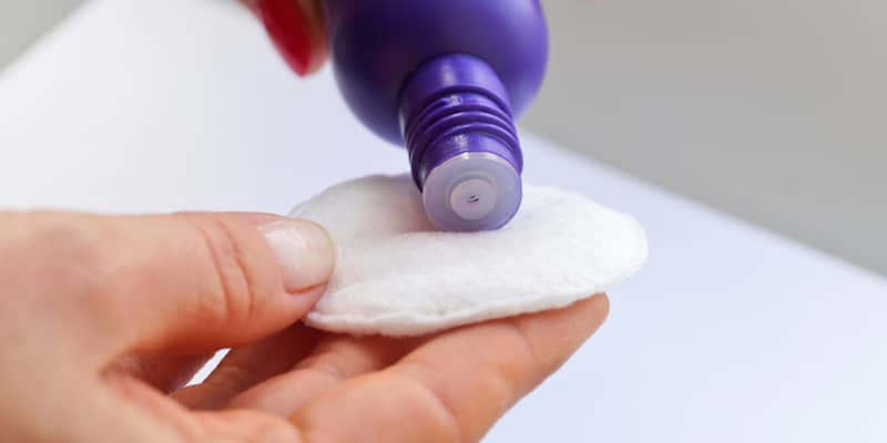 A woman's hand applies the nail polish remover on a cotton swab