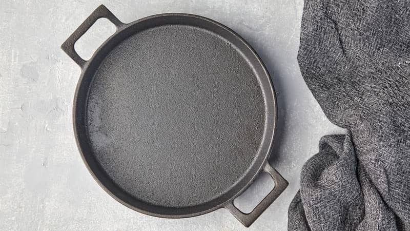 Black cast iron empty frying pan and gray kitchen towe