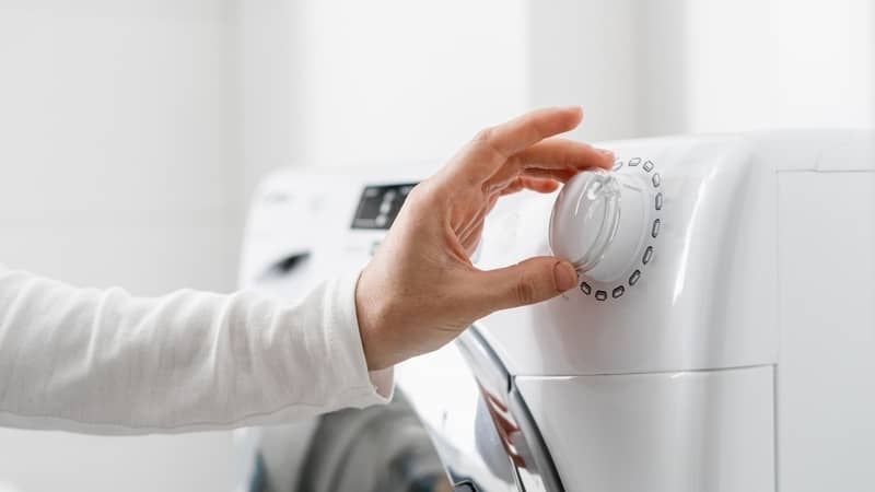 woman's hand adjusting the knob of a front load washing machine