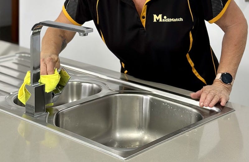 Professional cleaner cleaning a stainless steel sink in a customer's kitchen