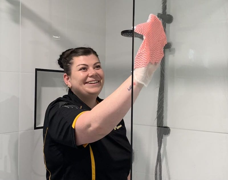 smiling cleaner wiping shower glass