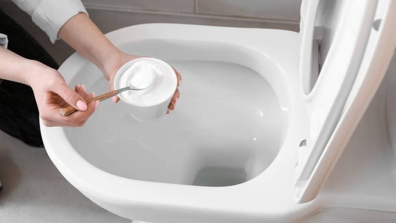 Woman cleaning white toilet bowl with baking soda