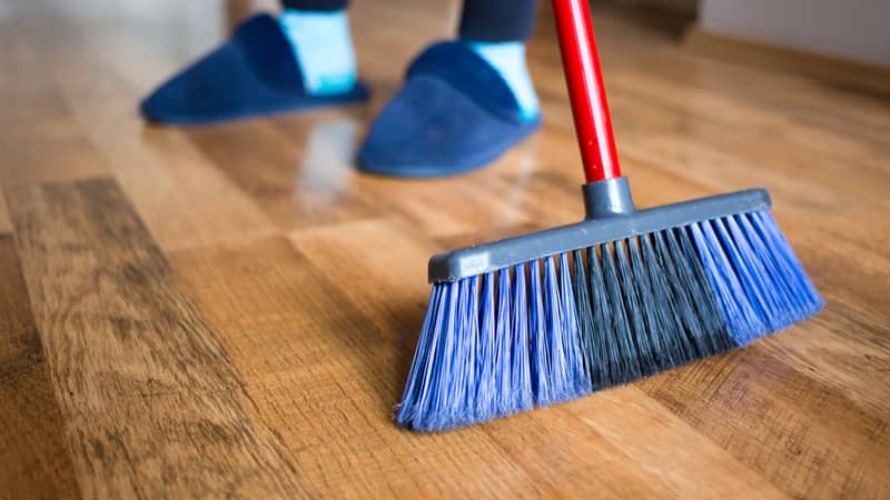 wife in blue slippers using indoor blue broom for hardwood floor cleaning. 