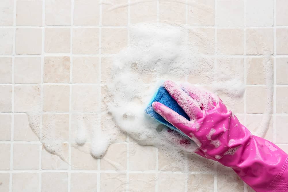 Woman in glove cleaning tile with sponge and foam