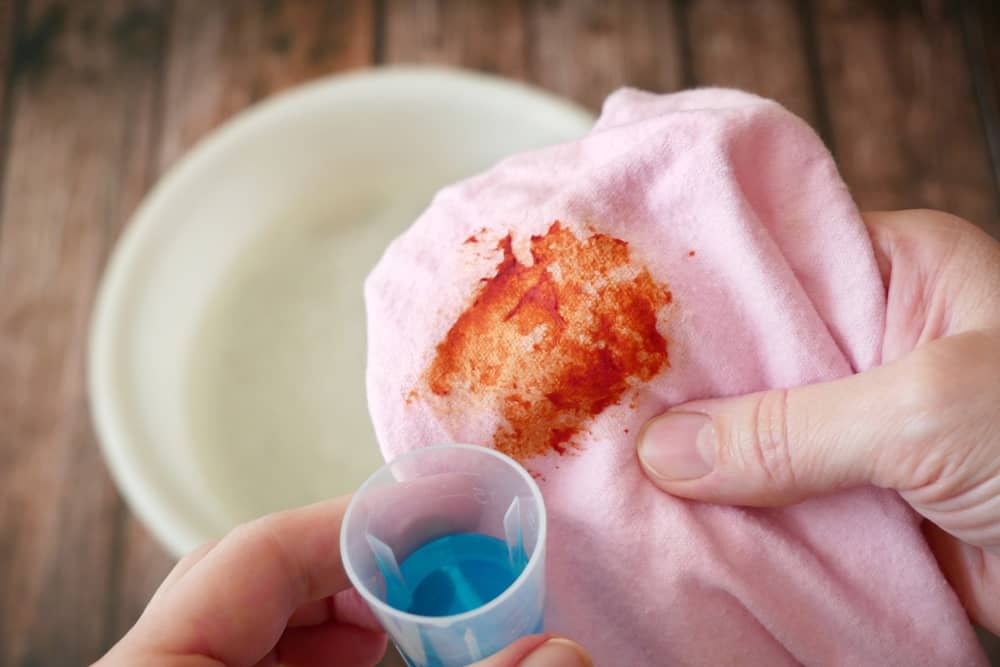 Women's hands washing dirty stained on colored cloth with a stain remover and soak in soapy water, closeup