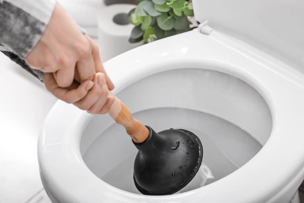 Hands using plunger to unclog a toilet bowl