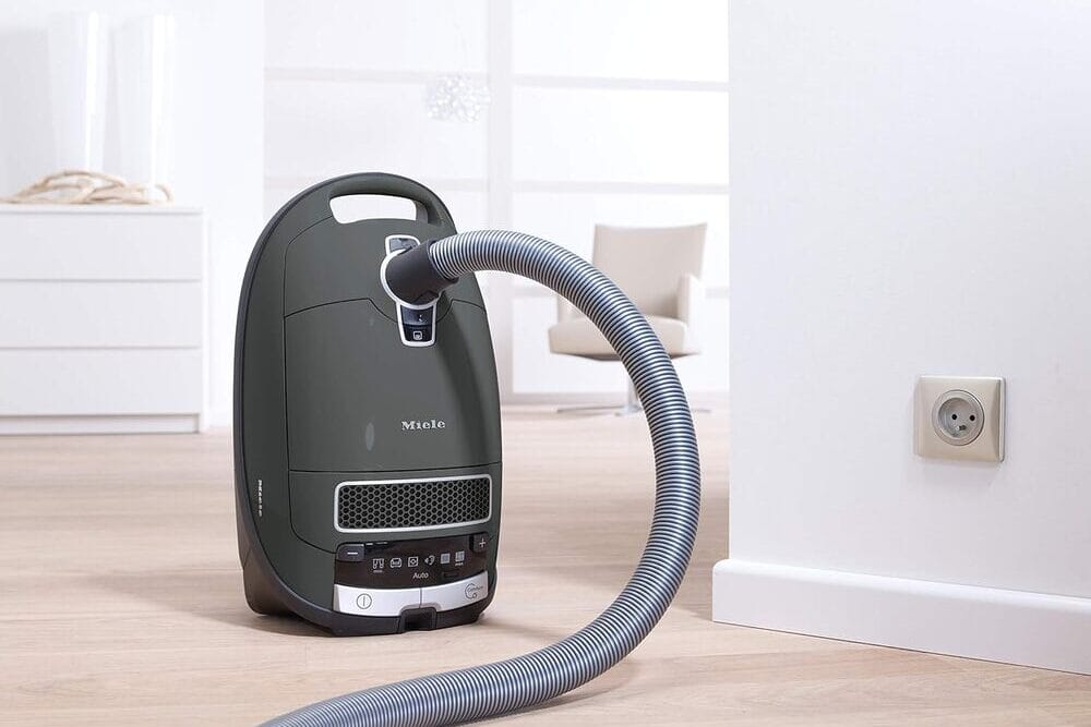 Modern Miele vacuum cleaner with flexible hose placed on a wooden floor