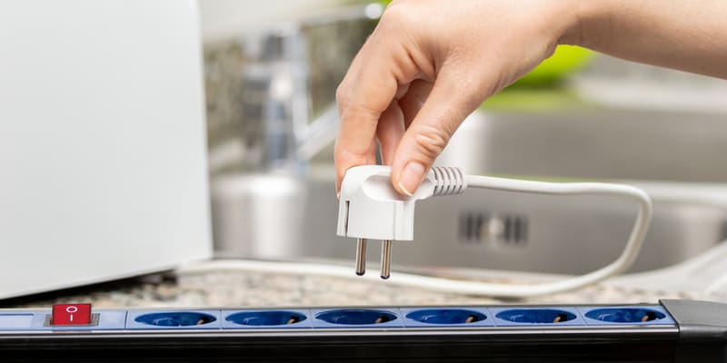 Close up of a woman's hand unplugging a toaster into the electrical outlet in a socket on a kitchen counter at home