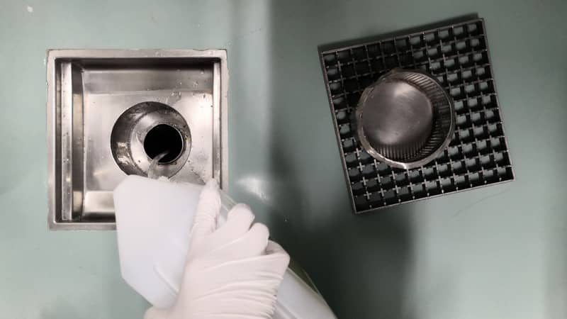 Removal of blockage in floor drain, the hand of a man with a bottle of drain cleaner.