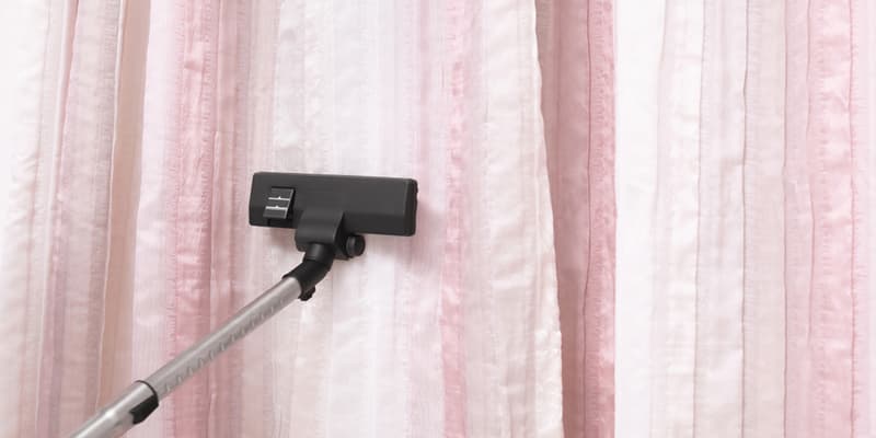 Removing dust from beautiful curtains with professional vacuum cleaner